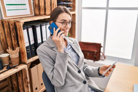 Téléchargez les photos : Young caucasian woman business worker talking on smartphone reading notebook at office - en image libre de droit