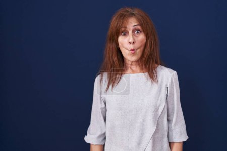 Photo for Middle age woman standing over blue background making fish face with lips, crazy and comical gesture. funny expression. - Royalty Free Image