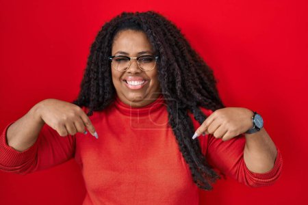Photo for Plus size hispanic woman standing over red background looking confident with smile on face, pointing oneself with fingers proud and happy. - Royalty Free Image