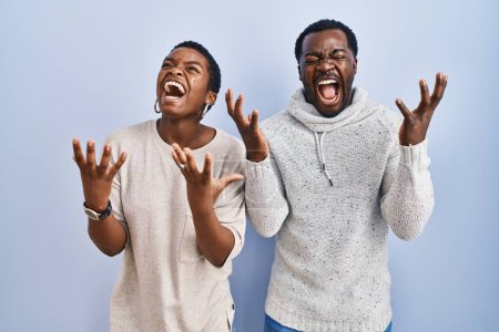 Téléchargez les photos : Jeune couple afro-américain debout sur fond bleu ensemble célébrer fou et fou de succès avec les bras levés et les yeux fermés hurlant excité. concept gagnant - en image libre de droit