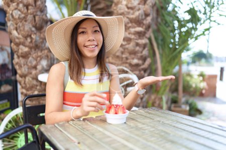 Photo for Middle age chinese woman eating ice cream outdoors at a terrace celebrating achievement with happy smile and winner expression with raised hand - Royalty Free Image