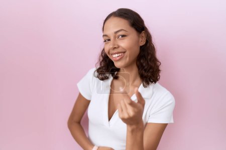 Téléchargez les photos : Jeune femme hispanique portant un t-shirt blanc décontracté signe venir ici geste avec la main invitant accueillant heureux et souriant - en image libre de droit