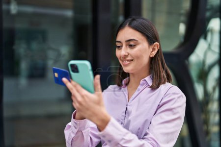 Photo for Young hispanic woman using smartphone and credit card at street - Royalty Free Image