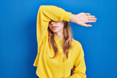 Photo for Young caucasian woman standing over blue background covering eyes with arm, looking serious and sad. sightless, hiding and rejection concept - Royalty Free Image