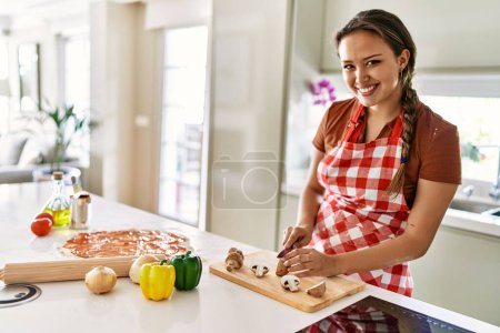 Photo for Young beautiful hispanic woman smiling confident cutting mushroom at the kitchen - Royalty Free Image
