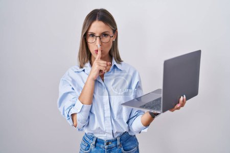 Téléchargez les photos : Jeune femme travaillant à l'aide d'un ordinateur portable demandant à être silencieux avec le doigt sur les lèvres. silence et concept secret. - en image libre de droit