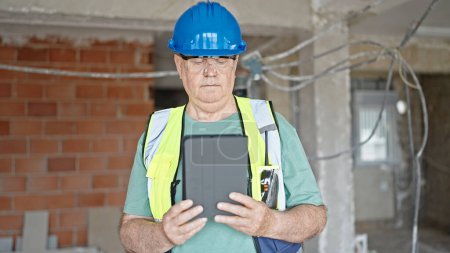 Photo for Middle age grey-haired man builder holding touchpad with relaxed expression at construction site - Royalty Free Image
