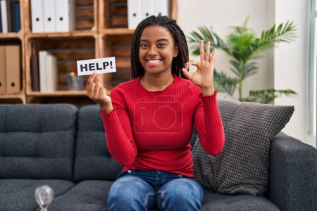 Foto de Joven afroamericano con trenzas haciendo terapia sosteniendo banner de ayuda haciendo signo de bien con los dedos, sonriendo gesto amistoso excelente símbolo - Imagen libre de derechos