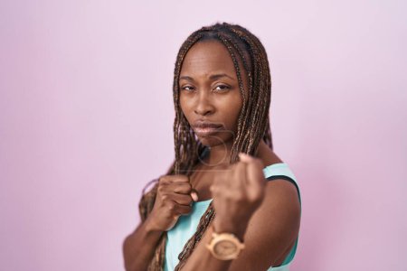 Téléchargez les photos : Femme afro-américaine debout sur fond rose prêt à se battre avec geste de défense poing, visage en colère et bouleversé, peur du problème - en image libre de droit