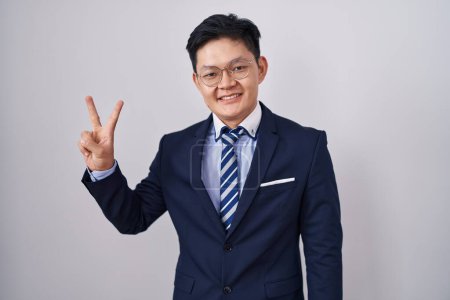 Foto de Joven asiático hombre vistiendo traje de negocios y corbata mostrando y apuntando hacia arriba con los dedos número dos mientras sonríe confiado y feliz. - Imagen libre de derechos