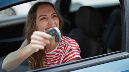 Téléchargez les photos : Jeune femme blonde souriante confiante tenant la clé de la nouvelle voiture à la rue - en image libre de droit