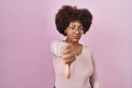 Foto de Joven mujer afroamericana de pie sobre fondo rosa mirando infeliz y enojado mostrando rechazo y negativo con los pulgares hacia abajo gesto. mala expresión. - Imagen libre de derechos