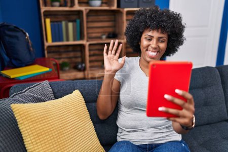 Photo for Black woman with curly hair using touchpad sitting on the sofa looking positive and happy standing and smiling with a confident smile showing teeth - Royalty Free Image
