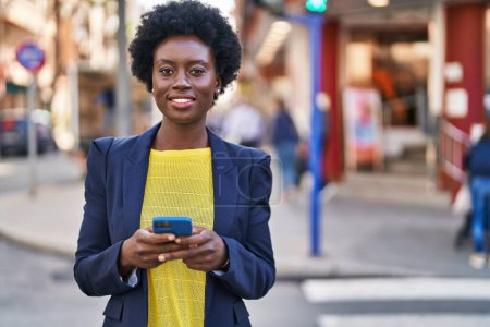 Téléchargez les photos : Jeune dirigeante d'entreprise afro-américaine utilisant un smartphone dans la rue - en image libre de droit