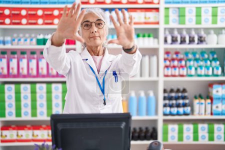 Photo for Middle age woman with tattoos working at pharmacy drugstore doing frame using hands palms and fingers, camera perspective - Royalty Free Image