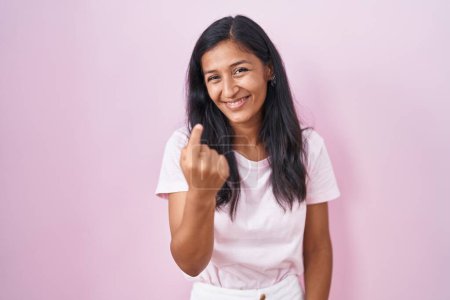 Photo for Young hispanic woman standing over pink background beckoning come here gesture with hand inviting welcoming happy and smiling - Royalty Free Image