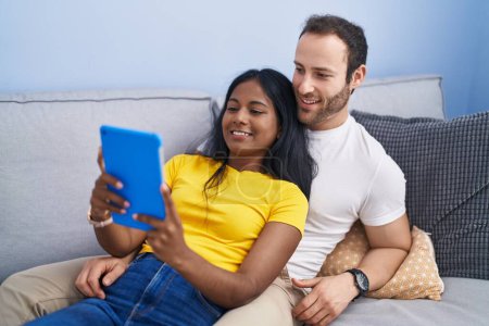 Téléchargez les photos : Man and woman interracial couple using touchpad lying on sofa at home - en image libre de droit