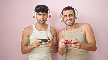 Photo for Two men playing video game with relaxed expression over isolated pink background - Royalty Free Image