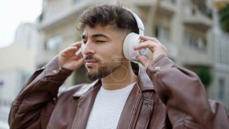 Foto de Hombre árabe joven escuchando música con expresión relajada en la calle - Imagen libre de derechos