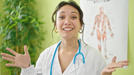 Foto de Joven hermosa mujer hispana doctora sonriendo confiada hablando en la clínica - Imagen libre de derechos