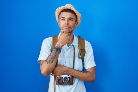 Photo for Brazilian young man holding vintage camera looking confident at the camera with smile with crossed arms and hand raised on chin. thinking positive. - Royalty Free Image