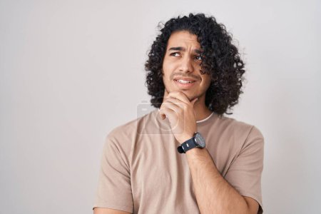 Photo for Hispanic man with curly hair standing over white background thinking worried about a question, concerned and nervous with hand on chin - Royalty Free Image