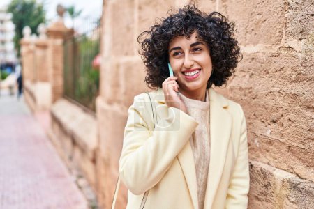Foto de Joven mujer de Oriente Medio excusa sonriendo confiado hablando en el teléfono inteligente en la calle - Imagen libre de derechos