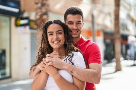 Foto de Joven pareja hispana sonriendo confiada abrazándose en la calle - Imagen libre de derechos