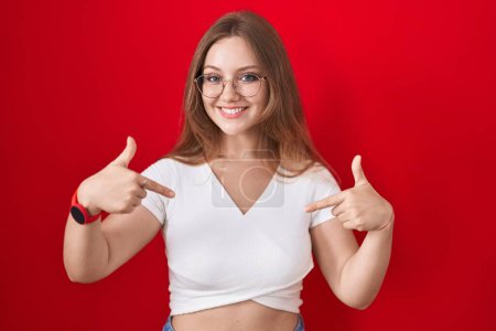 Photo for Young caucasian woman standing over red background looking confident with smile on face, pointing oneself with fingers proud and happy. - Royalty Free Image