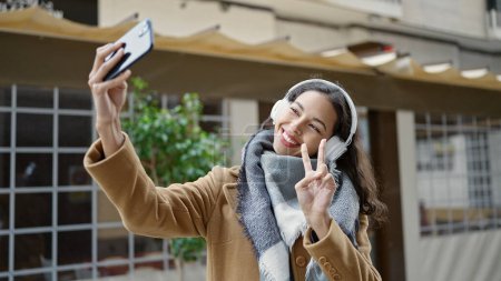 Téléchargez les photos : Jeune belle femme hispanique écoutant de la musique faire du selfie par smartphone sur la terrasse du café - en image libre de droit