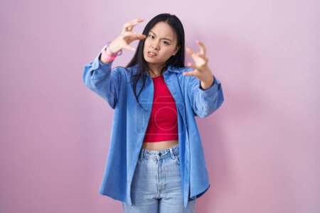 Photo for Young asian woman standing over pink background shouting frustrated with rage, hands trying to strangle, yelling mad - Royalty Free Image