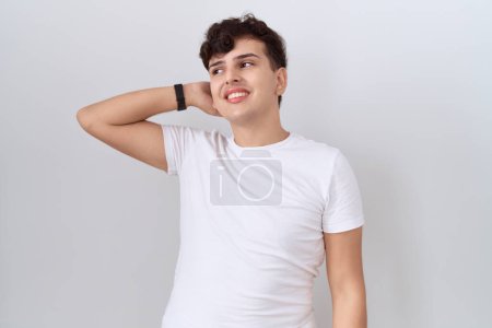 Téléchargez les photos : Jeune homme non binaire portant casual t-shirt blanc souriant confiant toucher les cheveux avec geste de la main vers le haut, posant attrayant et à la mode - en image libre de droit