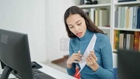 Photo for Young beautiful hispanic woman showing paper on video call at university classroom - Royalty Free Image