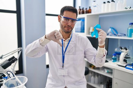 Photo for Young hispanic man with beard working at scientist laboratory holding blue ribbon with angry face, negative sign showing dislike with thumbs down, rejection concept - Royalty Free Image