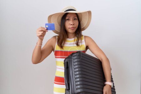Téléchargez les photos : Middle age chinese woman holding suitcase and credit card skeptic and nervous, frowning upset because of problem. negative person. - en image libre de droit