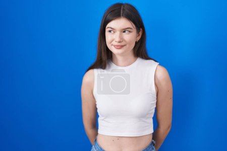 Téléchargez les photos : Jeune femme caucasienne debout sur fond bleu souriant regardant vers le côté et regardant loin en pensant. - en image libre de droit