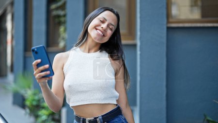 Photo for Young beautiful hispanic woman dancing listening to music on smartphone at street - Royalty Free Image