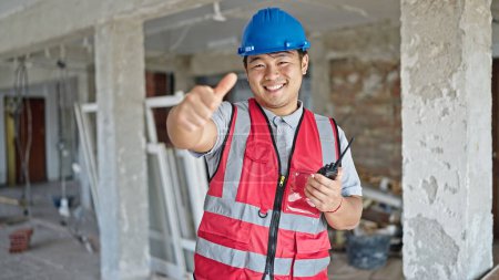 Foto de Constructor sonriendo confiado haciendo gesto pulgar hacia arriba en el sitio de construcción - Imagen libre de derechos