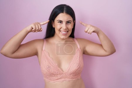 Photo for Young hispanic woman wearing pink bra smiling pointing to head with both hands finger, great idea or thought, good memory - Royalty Free Image