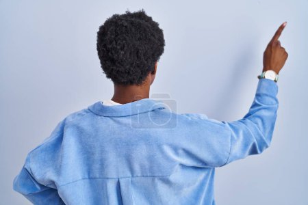 Photo for African american woman standing over blue background posing backwards pointing ahead with finger hand - Royalty Free Image
