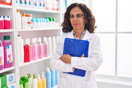 Téléchargez les photos : Pharmacien femme d'âge moyen tenant presse-papiers à la pharmacie - en image libre de droit