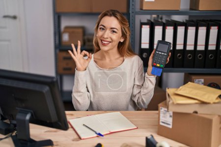 Foto de Mujer hispana que trabaja en el comercio electrónico de pequeñas empresas con tarjeta de crédito y datáfono haciendo signo bien con los dedos, sonriendo gesto amistoso excelente símbolo - Imagen libre de derechos