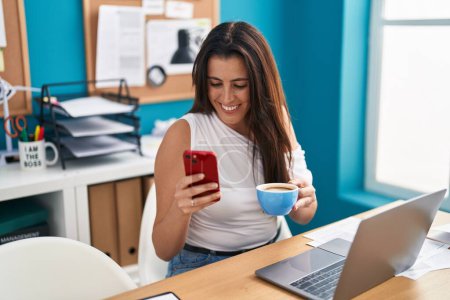 Foto de Joven hermosa mujer hispana trabajadora de negocios usando smartphone bebiendo café en la oficina - Imagen libre de derechos