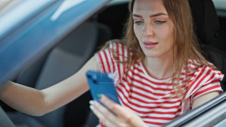 Téléchargez les photos : Jeune femme blonde utilisant smartphone voiture de conduite à la rue - en image libre de droit