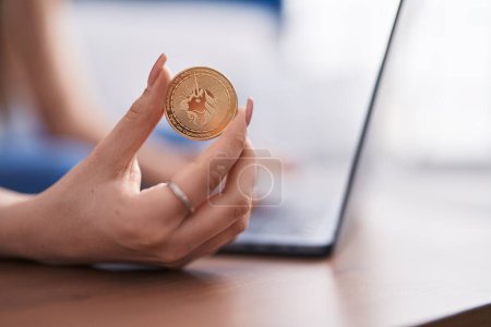 Photo for Young caucasian woman using laptop holding uniswap coin at home - Royalty Free Image