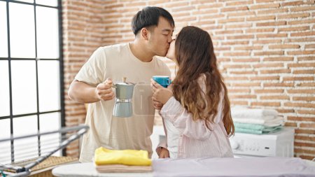 Foto de Hombre y mujer pareja planchando ropa sosteniendo café besándose en la lavandería - Imagen libre de derechos