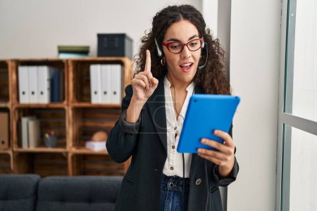 Foto de Young hispanic woman using touchpad wearing headphones smiling with an idea or question pointing finger with happy face, number one - Imagen libre de derechos