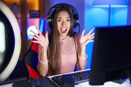 Photo for Young hispanic woman playing video games celebrating crazy and amazed for success with arms raised and open eyes screaming excited. winner concept - Royalty Free Image