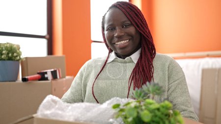 Téléchargez les photos : Femme africaine avec des cheveux tressés souriant paquet de maintien confiant à la nouvelle maison - en image libre de droit