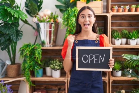 Photo for Young hispanic woman working at florist holding open sign screaming proud, celebrating victory and success very excited with raised arms - Royalty Free Image